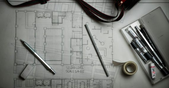 Architectural blueprints with drafting pencils and a metal ruler, illustrating Autodesk connecting desktop, mobile and cloud