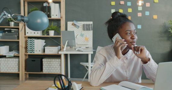 Woman talking on phone at desk in office, illustrating broadband and VoIP basics