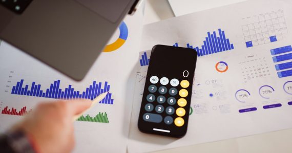 A calculator sitting on top of a table next to a laptop, illustrating cloud bringing IT budgets under control