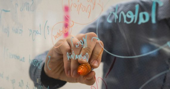 Person writing on glass whiteboard with diagrams, illustrating including the cloud in business strategy