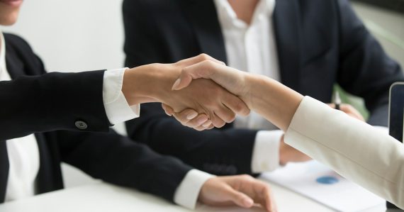 Two people shaking hands in front of a laptop, illustrating cloud computing and business success