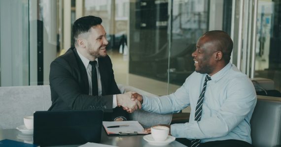 Two businessmen shaking hands across a table, illustrating business virtualization benefits