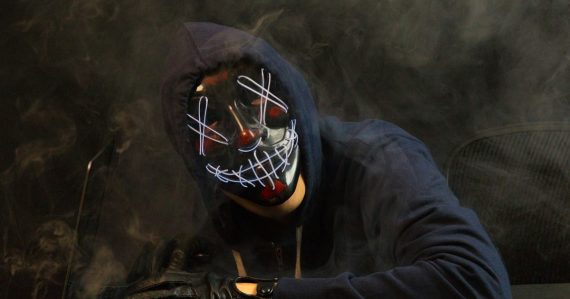 Hooded figure in a mask at a computer, illustrating cloud and BYOD network security threats