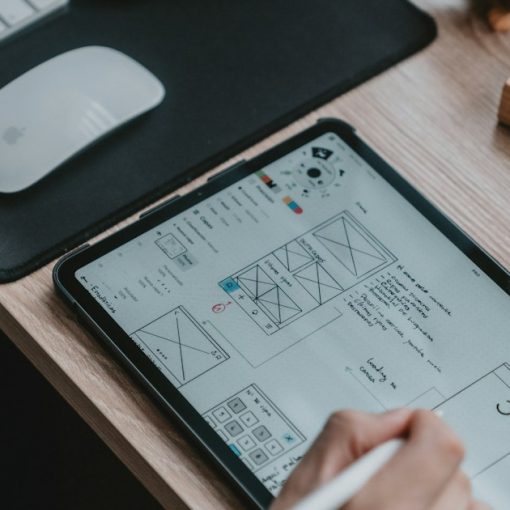 A person using a stylus on a tablet displaying wireframe sketches, illustrating mobile and cloud computing for CAD/CAM