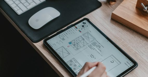 A person using a stylus on a tablet displaying wireframe sketches, illustrating mobile and cloud computing for CAD/CAM