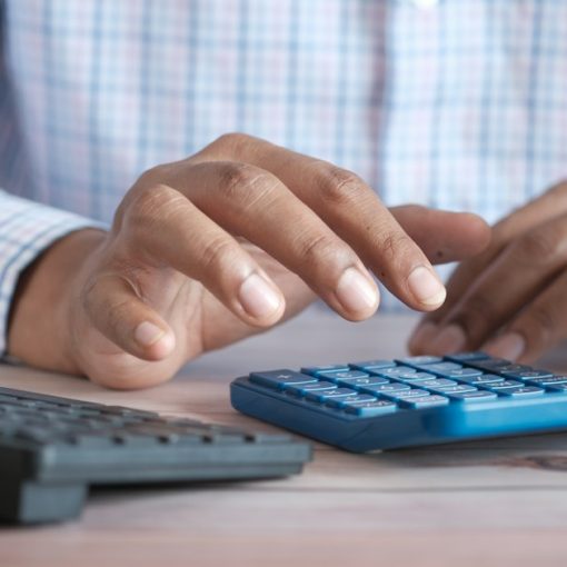 Person using calculator at desk with coffee mug, illustrating CFOs and cloud computing expectations