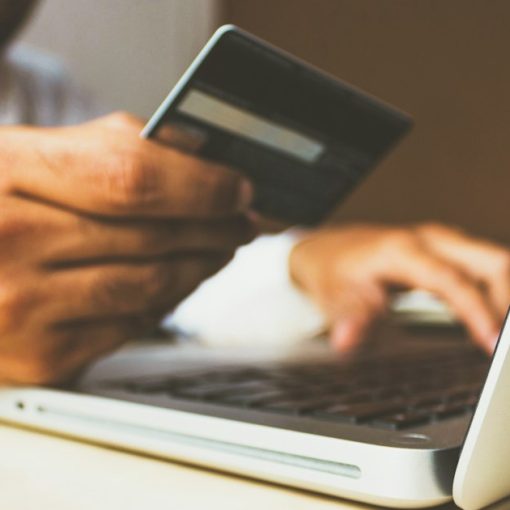 Person using a laptop while holding a payment card, illustrating users buying their own IT