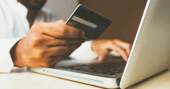 Person using a laptop while holding a payment card, illustrating users buying their own IT