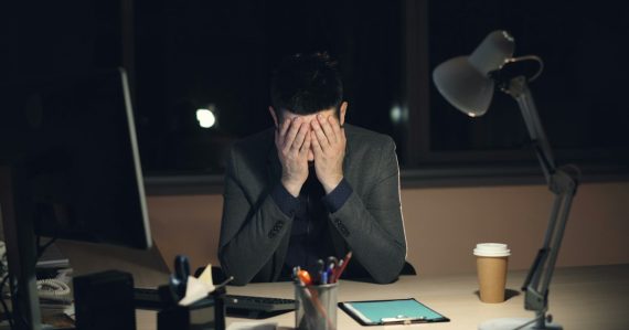 Man in suit sits at desk with head in hands, illustrating CIOs worried by cloud computing