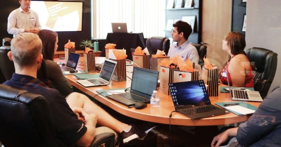 Man presenting to people seated at a table with laptops, illustrating defining cloud computing for the channel