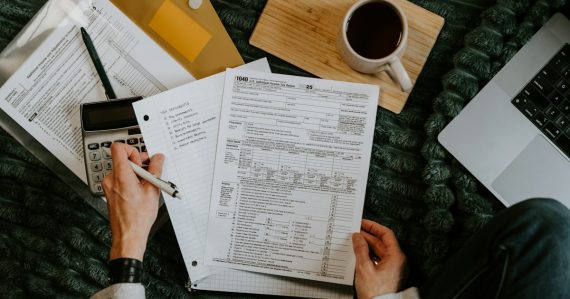 Person reviewing documents with calculator and laptop, illustrating cloud computing for accountants
