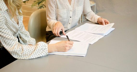 Woman signing documents beside a colleague, illustrating cloud computing contracts and services