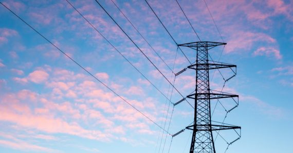 Black electric pylon under orange clouds, illustrating cloud computing compared to a power grid