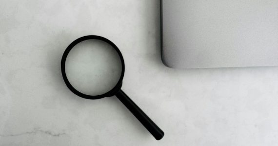 Magnifying glass sits near a laptop on a table, illustrating myths of cloud computing