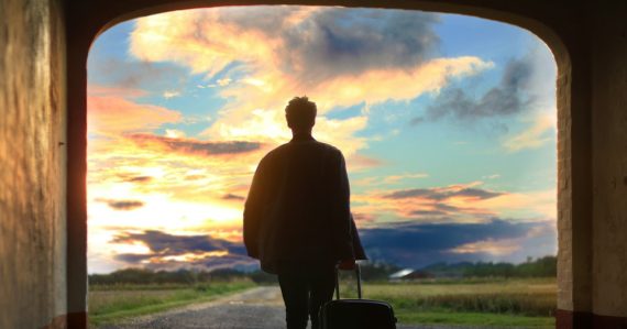 Business traveler with luggage watching a sunset at an airport window, illustrating cloud beyond IT