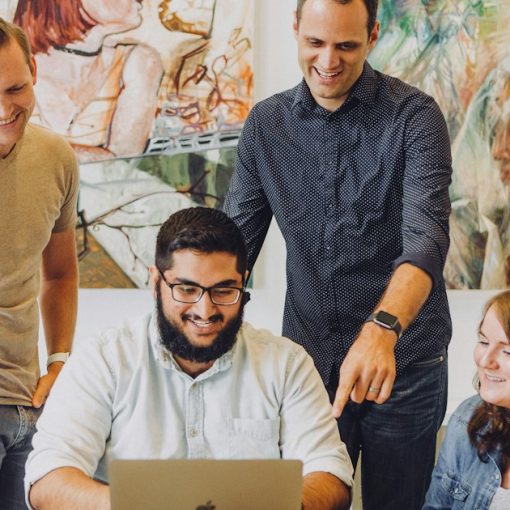 Four coworkers smiling around laptop at table, illustrating cloud computing versus outsourcing
