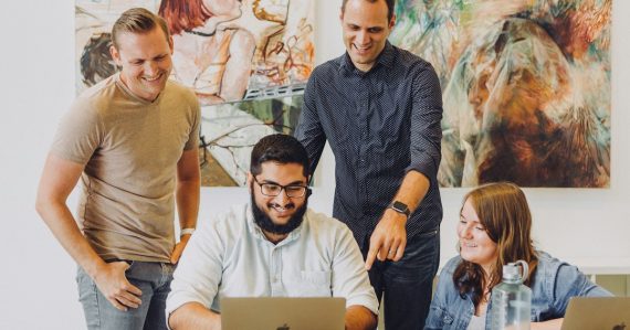 Four coworkers smiling around laptop at table, illustrating cloud computing versus outsourcing