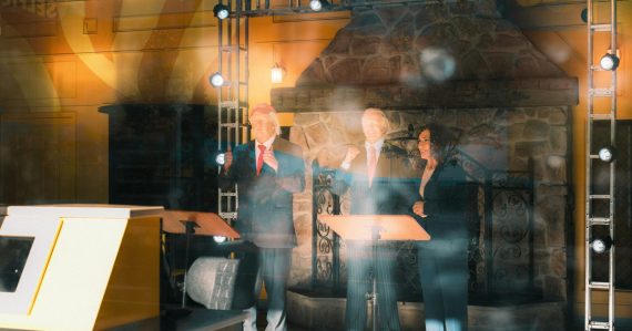 Three people stand behind podiums on a stage, illustrating the debate over cloud standards
