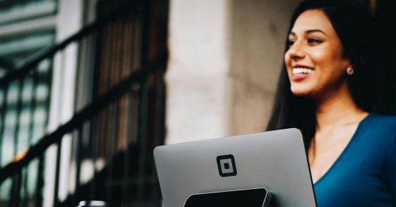 A woman smiling at a customer holding a coffee cup at a checkout, illustrating cloud economics and the customer experience