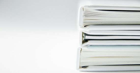 A stack of thick folders on a white surface, illustrating cloud governance beyond security