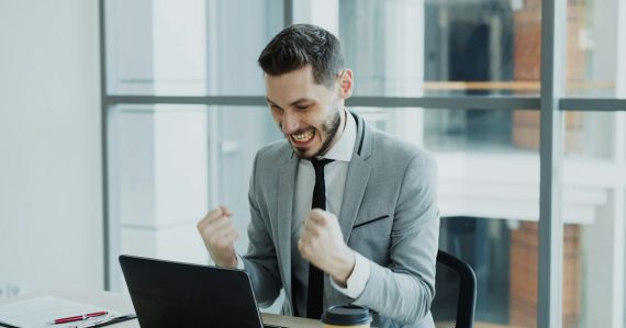 Businessman celebrating success at his laptop, illustrating cloud computing living up to the hype