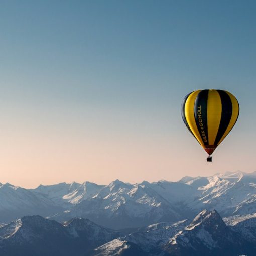 Yellow and blue hot air balloon flying over the mountains, illustrating lifting a business through cloud migration