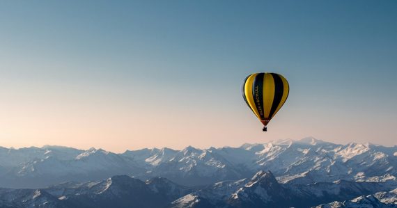 Yellow and blue hot air balloon flying over the mountains, illustrating lifting a business through cloud migration