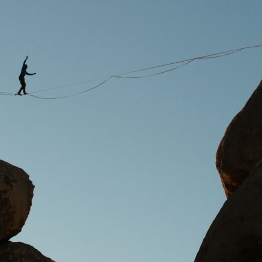 Person balances on tightrope between rock formations, illustrating managing cloud security risks