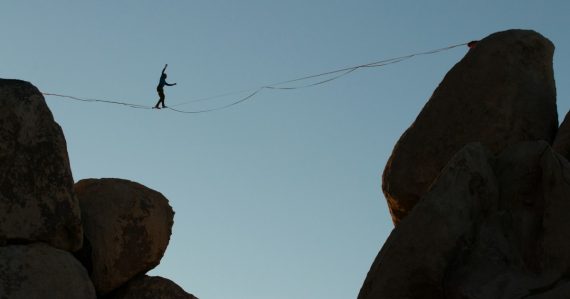 Person balances on tightrope between rock formations, illustrating managing cloud security risks