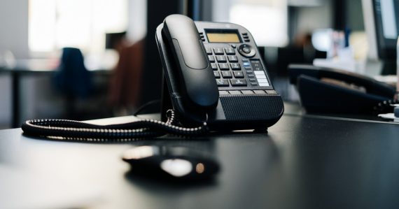 Black ip desk phone on black wooden table, illustrating cloud VoIP services