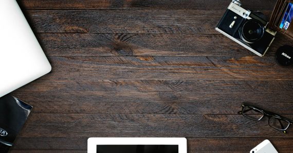 A laptop, tablet, smartphone, camera, and glasses on a dark wooden desk, illustrating IT consumerisation as an opportunity