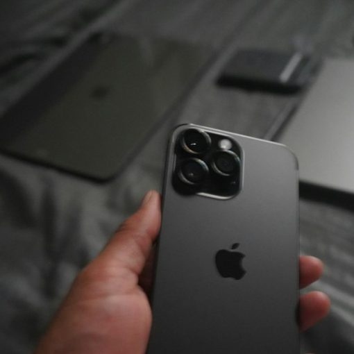 A hand holding a dark grey smartphone with a triple camera array, illustrating CIOs and the consumerization of IT