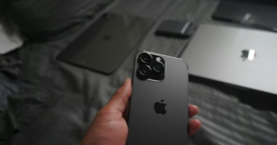 A hand holding a dark grey smartphone with a triple camera array, illustrating CIOs and the consumerization of IT