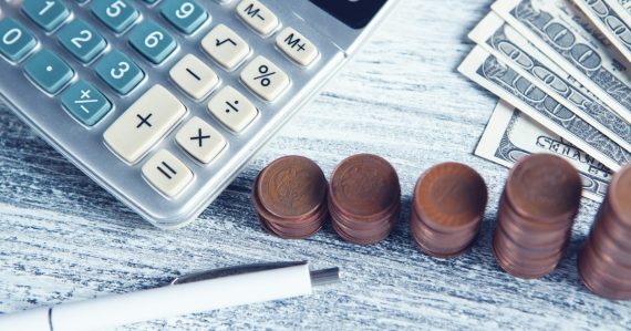 A calculator, pen, and money on a table, illustrating the cost advantage debate over cloud computing