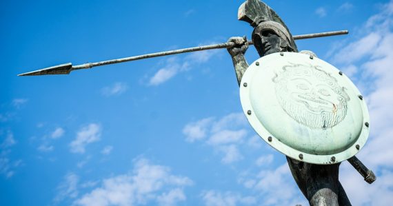 Bronze warrior statue with spear and shield under blue sky, illustrating defending the cloud after outages