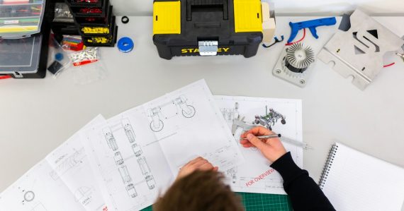 A person using a caliper to measure technical engineering drawings, illustrating cloud computing for design engineers