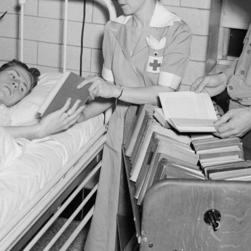 Nurse and soldier give books to patient in hospital bed, illustrating DoD desktop virtualization in healthcare