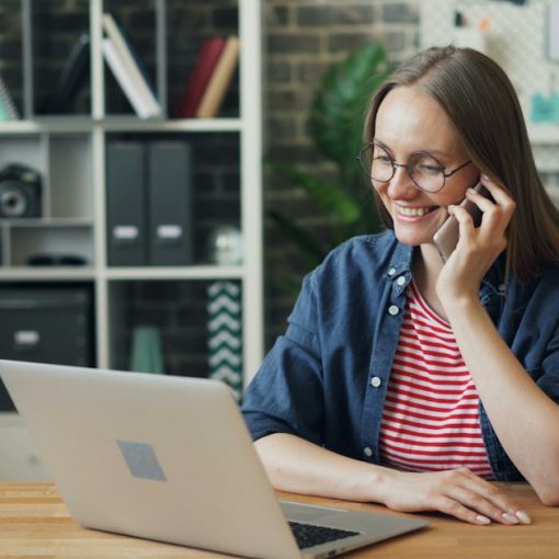 A woman talking on a cell phone while using a laptop, illustrating businesses considering VoIP