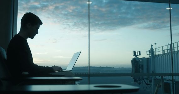 Man working on laptop by an airport window at sunrise, illustrating mobility driving desktop virtualization