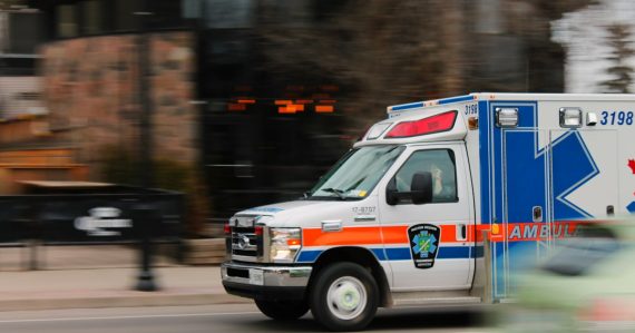 White and blue ambulance van traveling on road, illustrating E911 location for enterprise phone systems