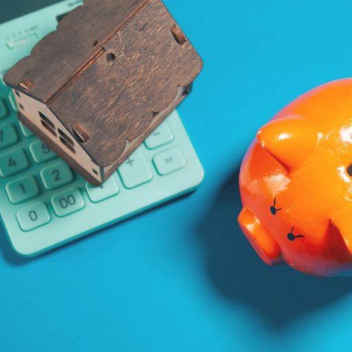 Calculator, piggy bank, and house model on blue background, illustrating an economic model for enterprise IT in the cloud