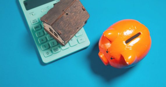 Calculator, piggy bank, and house model on blue background, illustrating an economic model for enterprise IT in the cloud