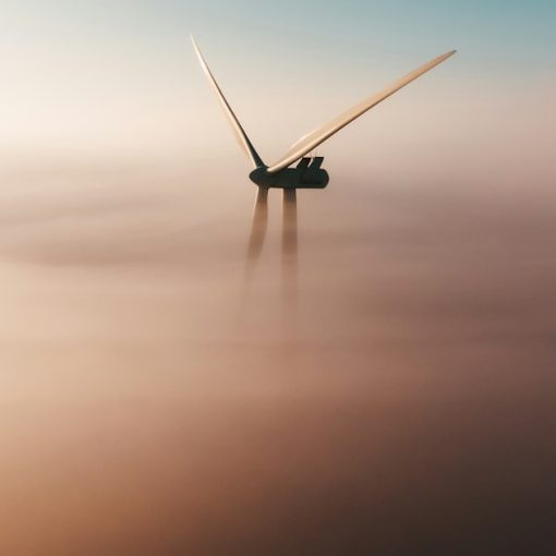 Wind turbine emerging from fog at sunrise, illustrating environmental benefits of cloud computing