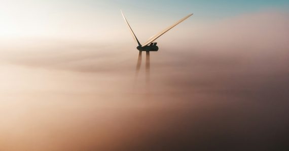 Wind turbine emerging from fog at sunrise, illustrating environmental benefits of cloud computing