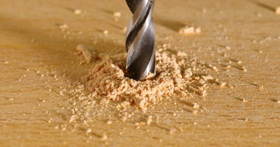 A drill being used to drill a piece of wood, illustrating business outcomes over technical specs