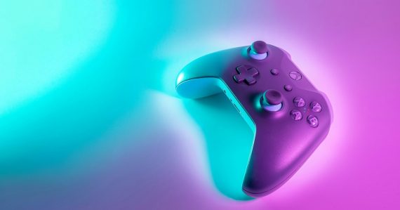 A wireless game controller lit by cyan and magenta neon light, illustrating cloud gaming power