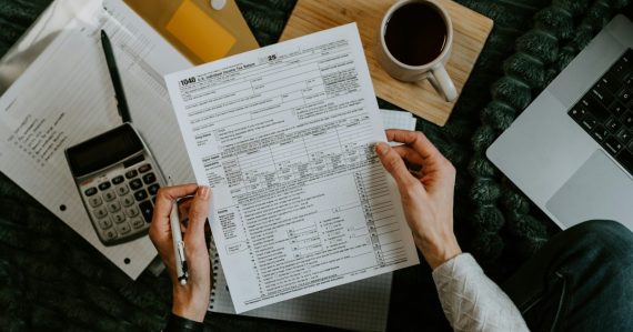 Hands holding tax forms with calculator and laptop, illustrating H&R Block's thin client virtualization