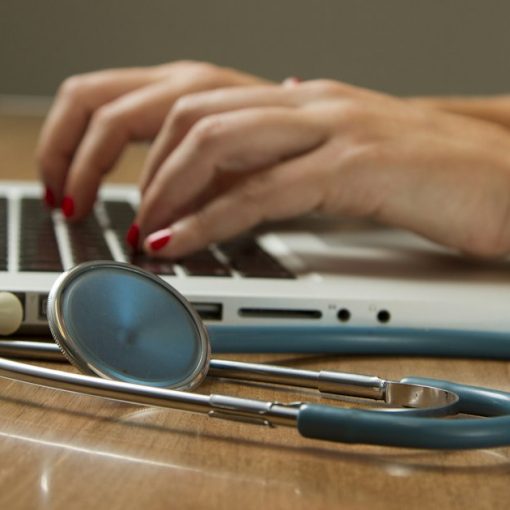 Person using laptop computer with a green stethoscope nearby, illustrating cloud computing in healthcare