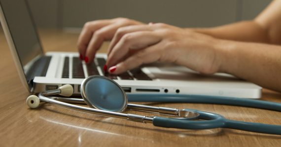 Person using laptop computer with a green stethoscope nearby, illustrating cloud computing in healthcare