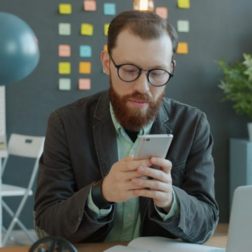 Man in glasses using smartphone at office desk, illustrating hosted PBX
